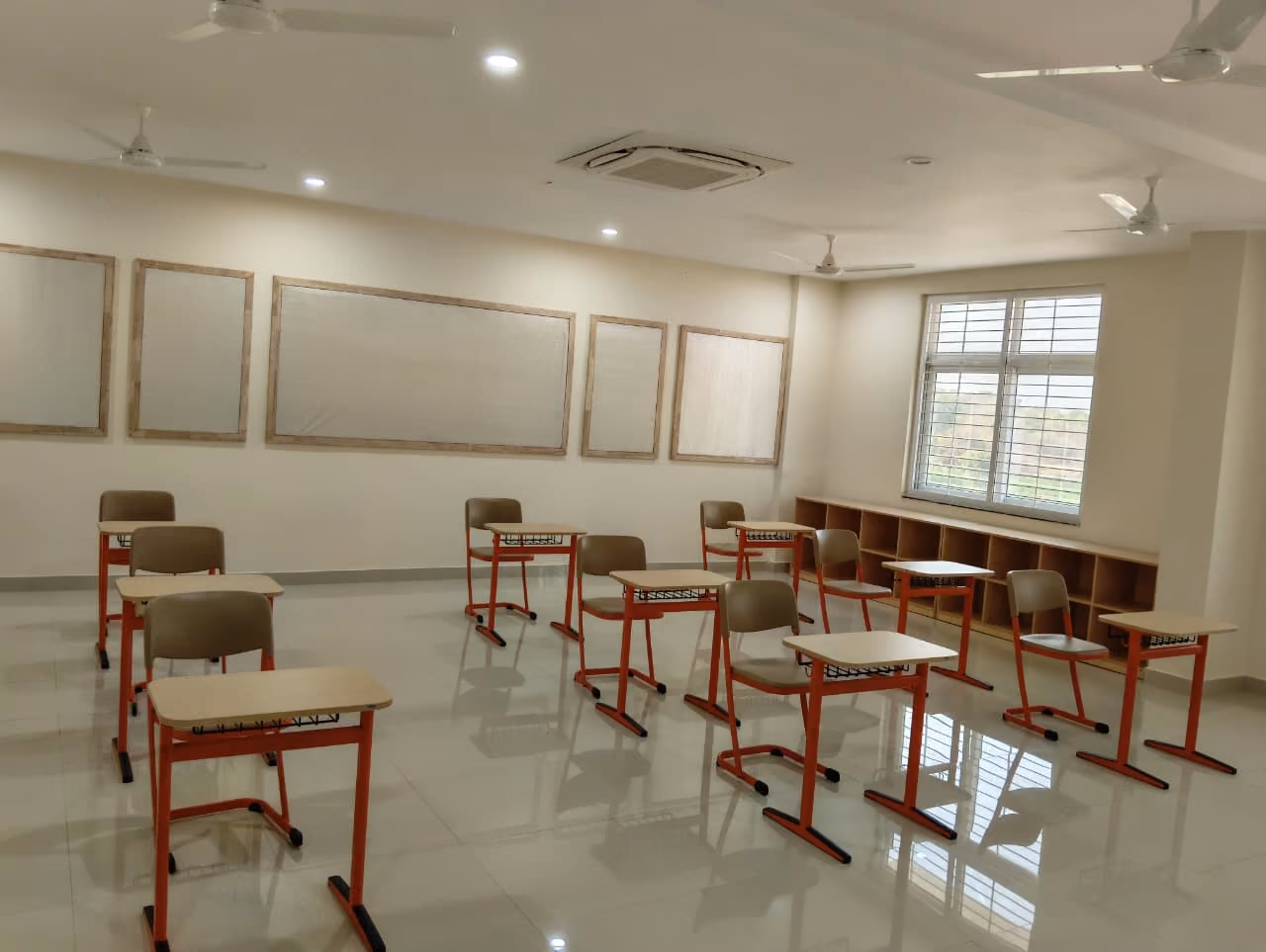 Modern classroom with orange-framed student desks, natural light, and ceiling fans