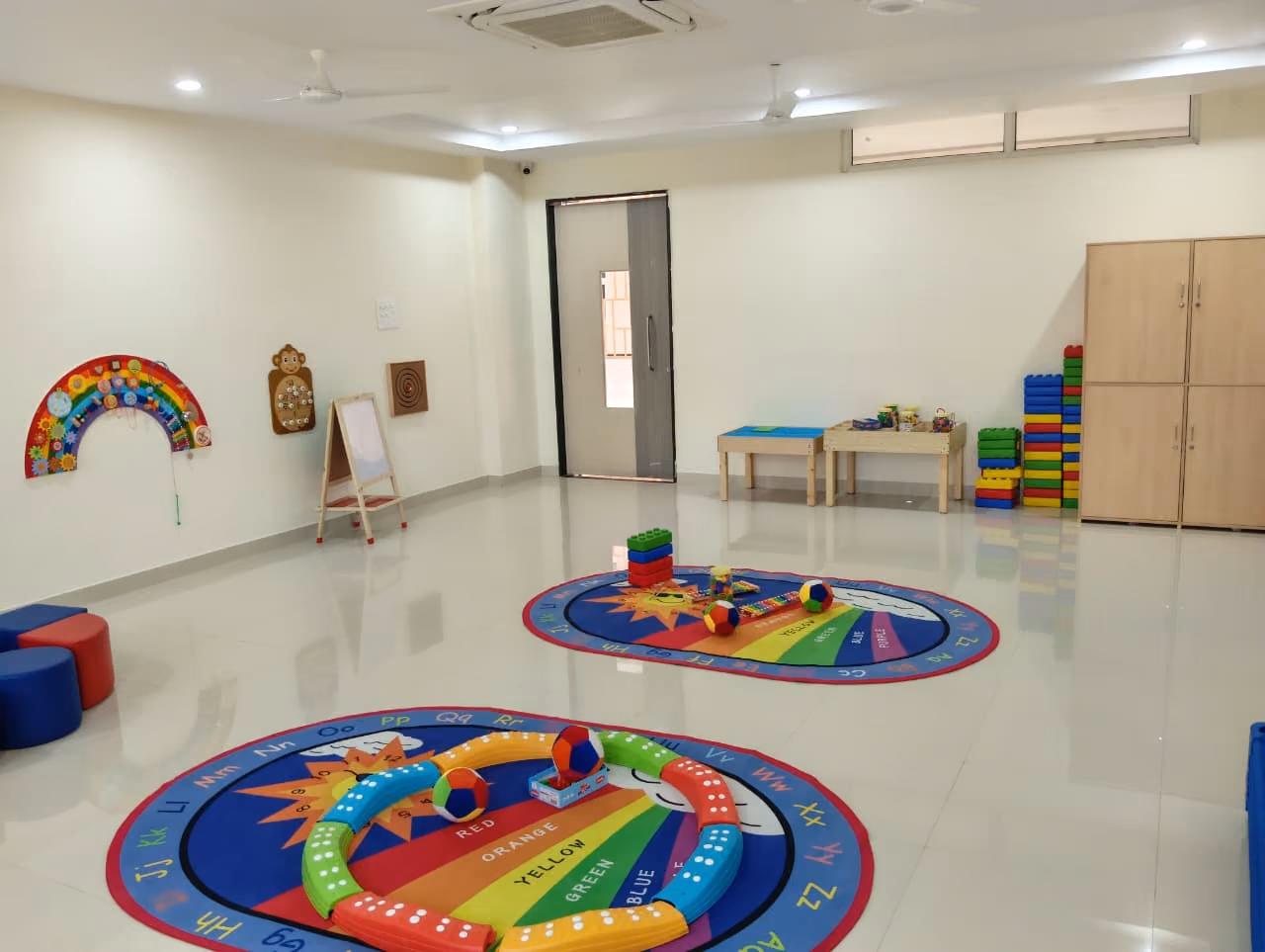 Early years room with alphabet rugs, soft play toys, and child-sized tables