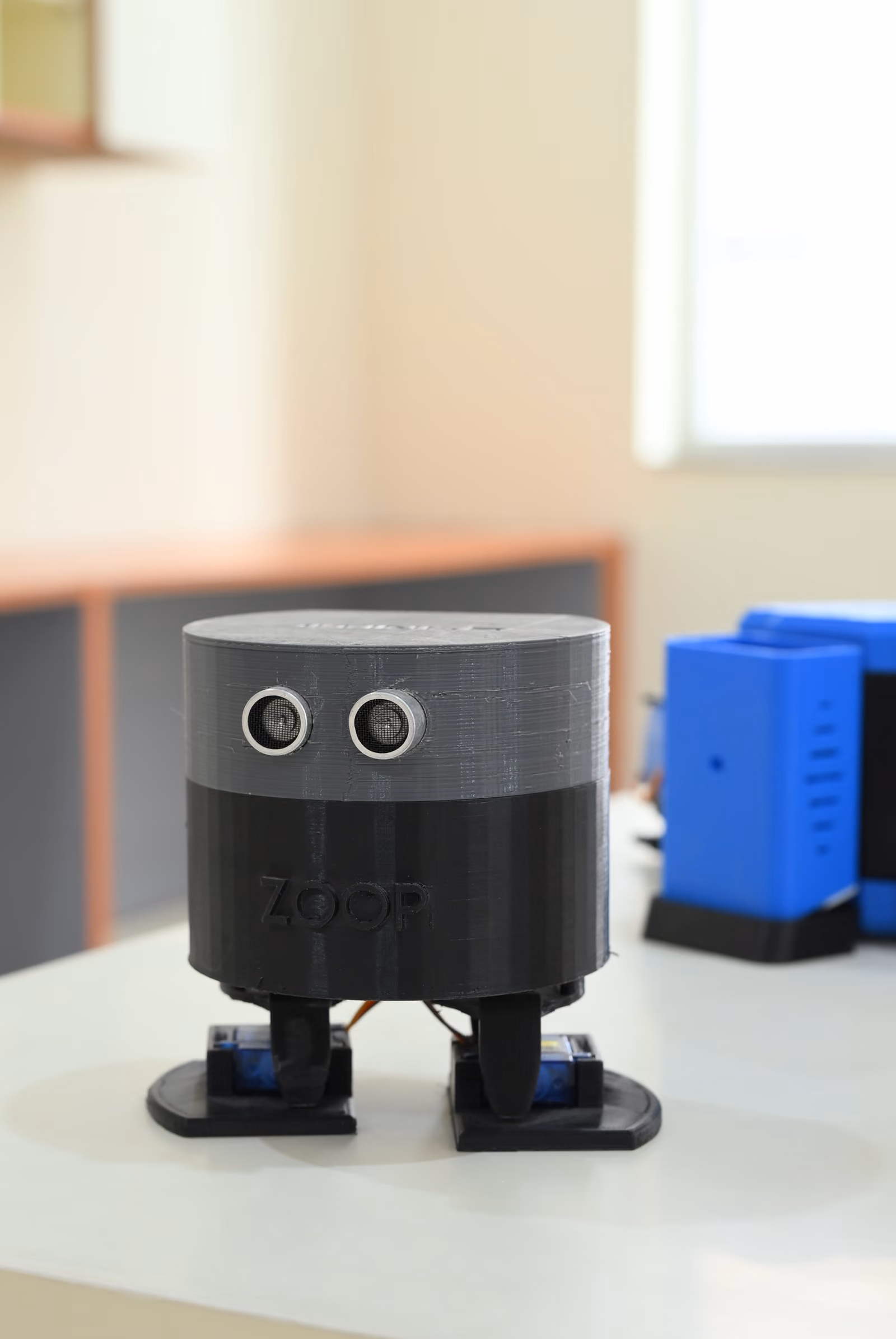 3D-printed bipedal robot named ZOOP with sensor eyes on a lab table