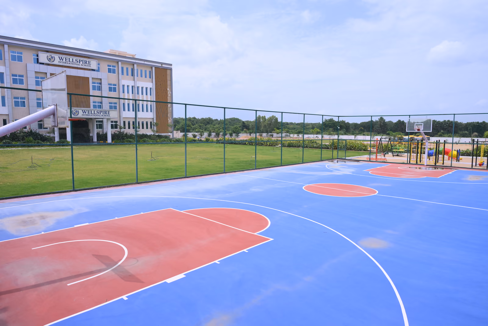 Outdoor blue and red basketball court with the school building beyond the fence